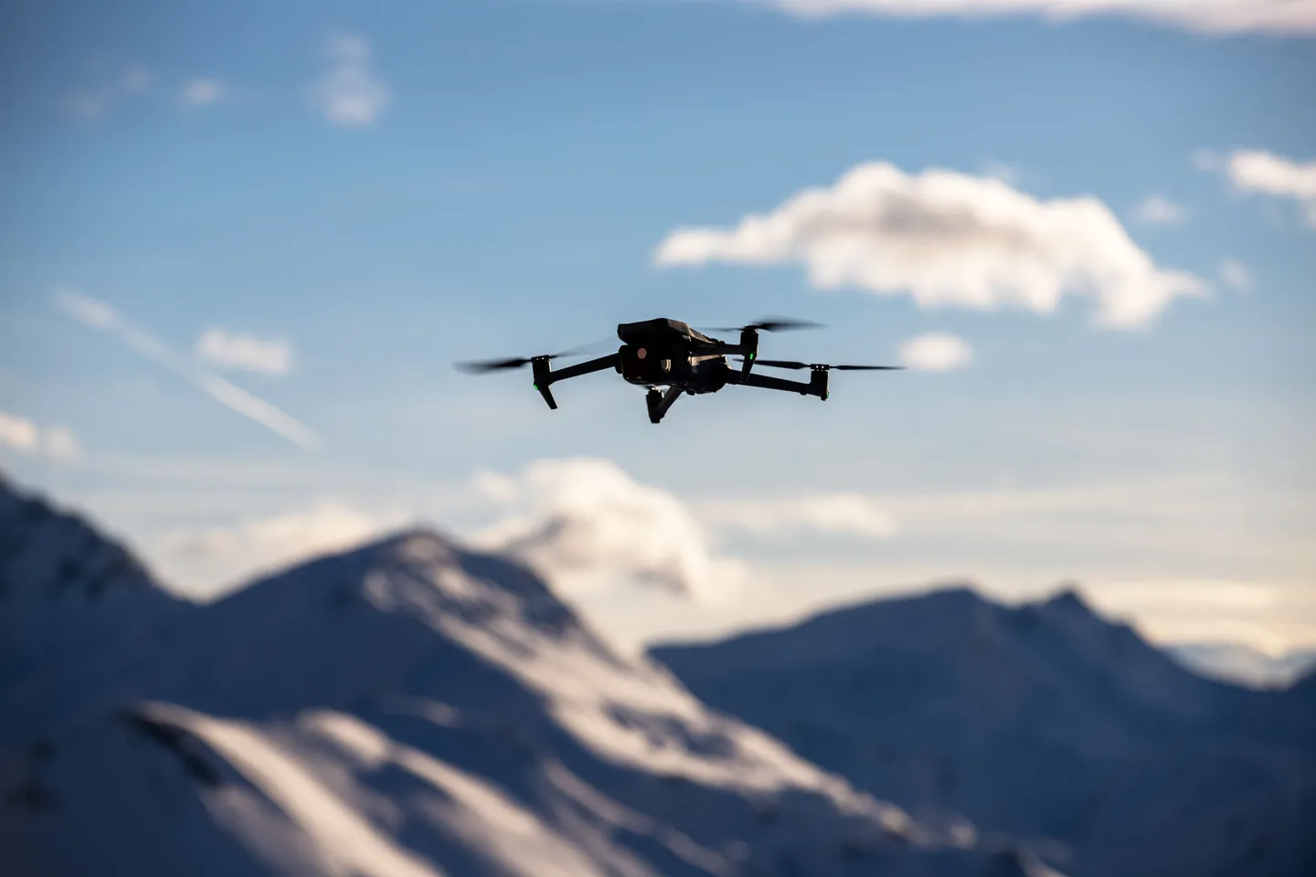 A drone hovering in the air against snowy mountain peaks and a blue sky