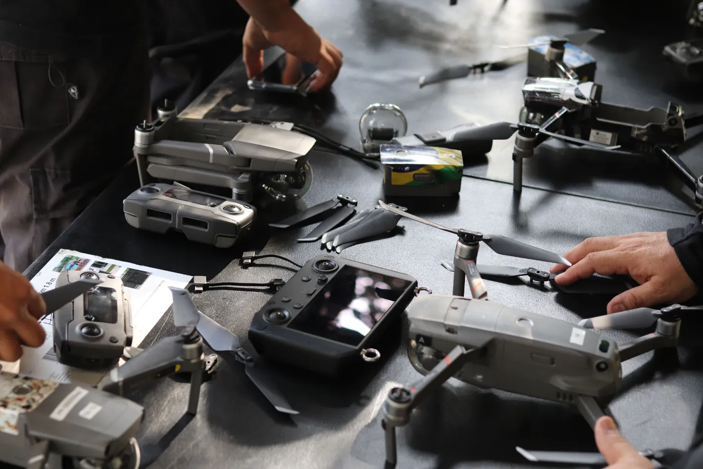 Hands setting up drones, controllers, and spare propellers on a table
