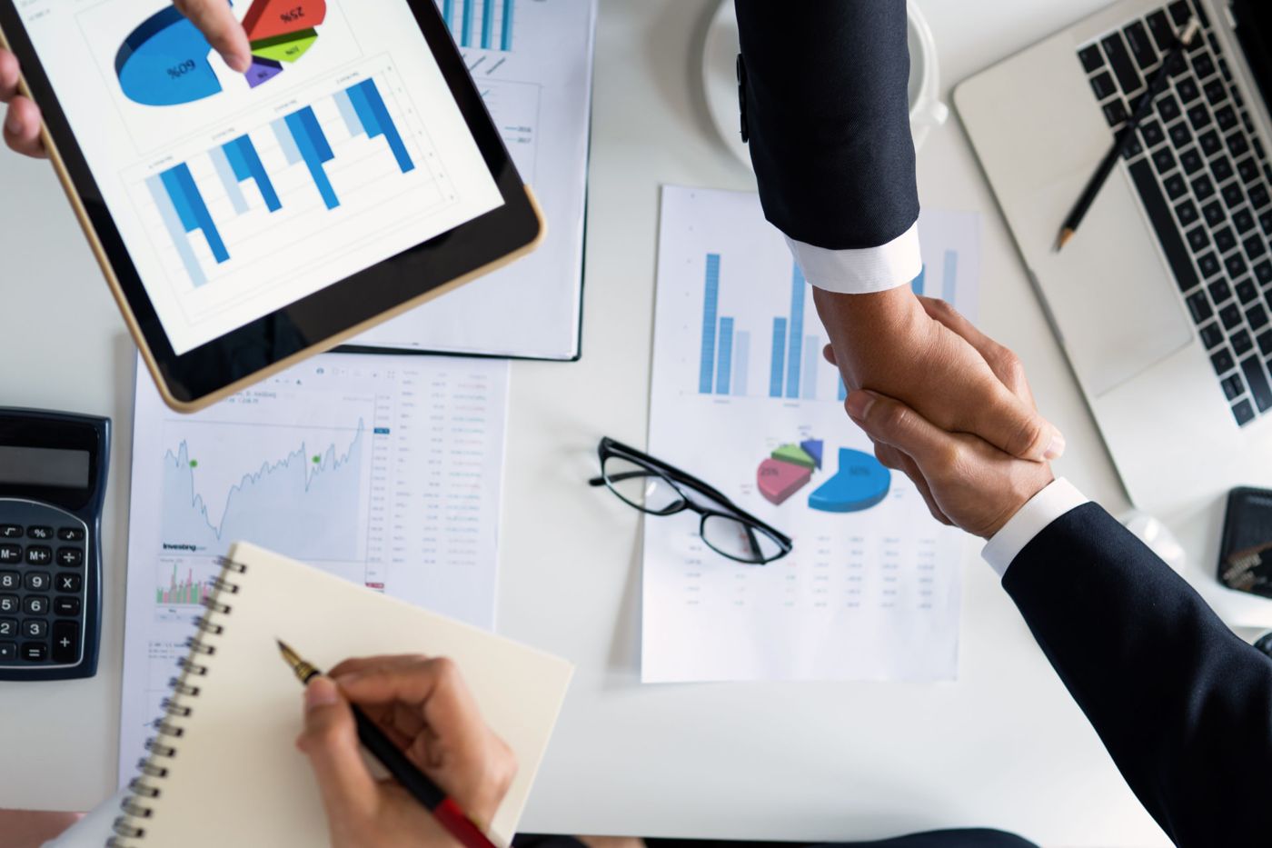 Two professionals shaking hands over charts and financial reports