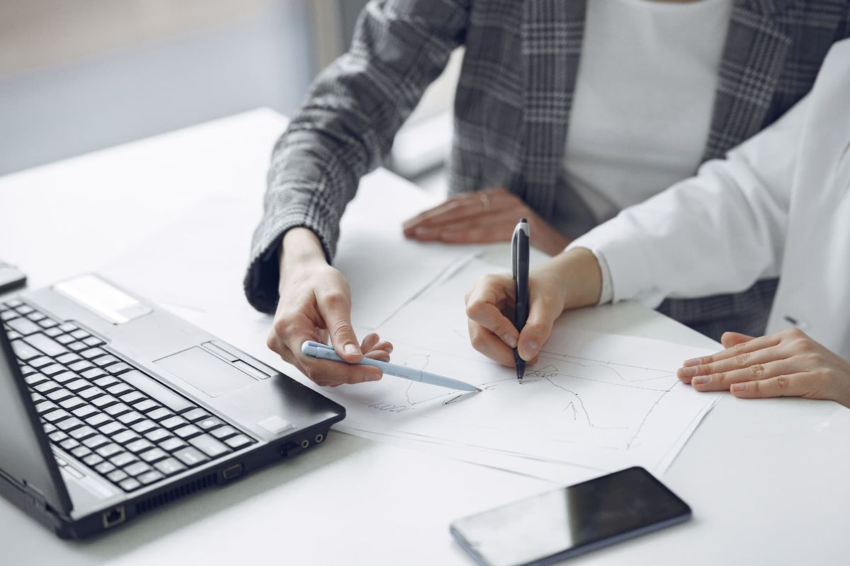 Two professionals mapping out a pricing plan on paper beside a laptop