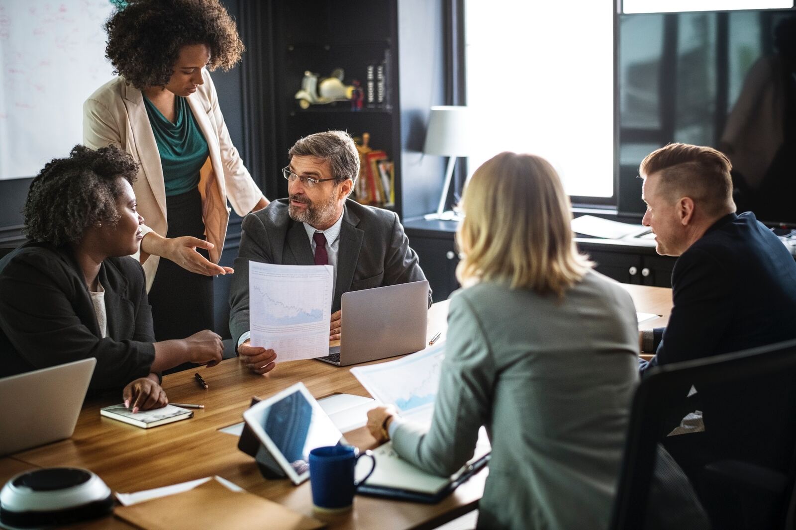 Cross-functional team meeting around a conference table reviewing reports and charts