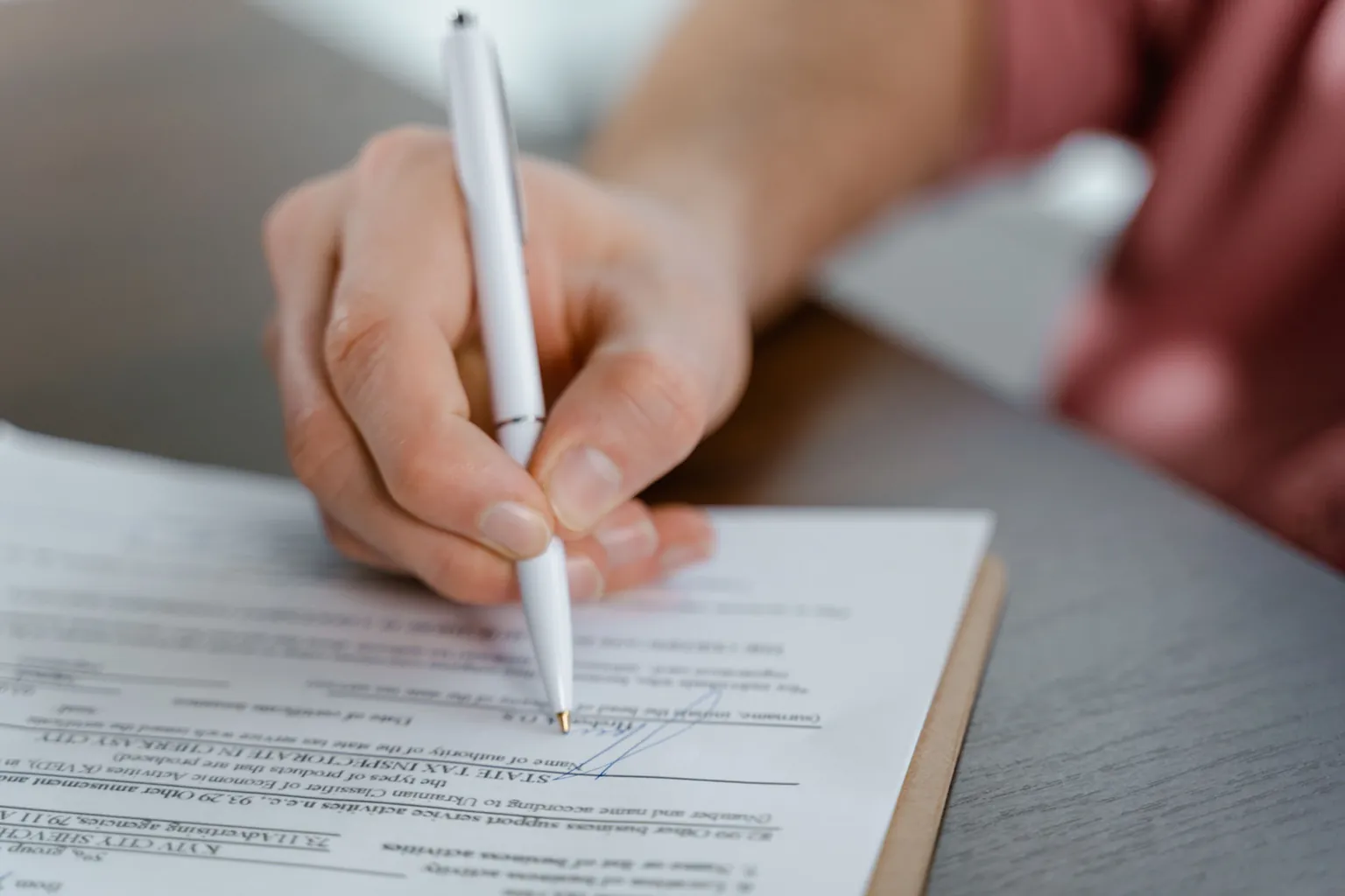 Close-up of a professional signing a business contract with a white pen on a clipboard
