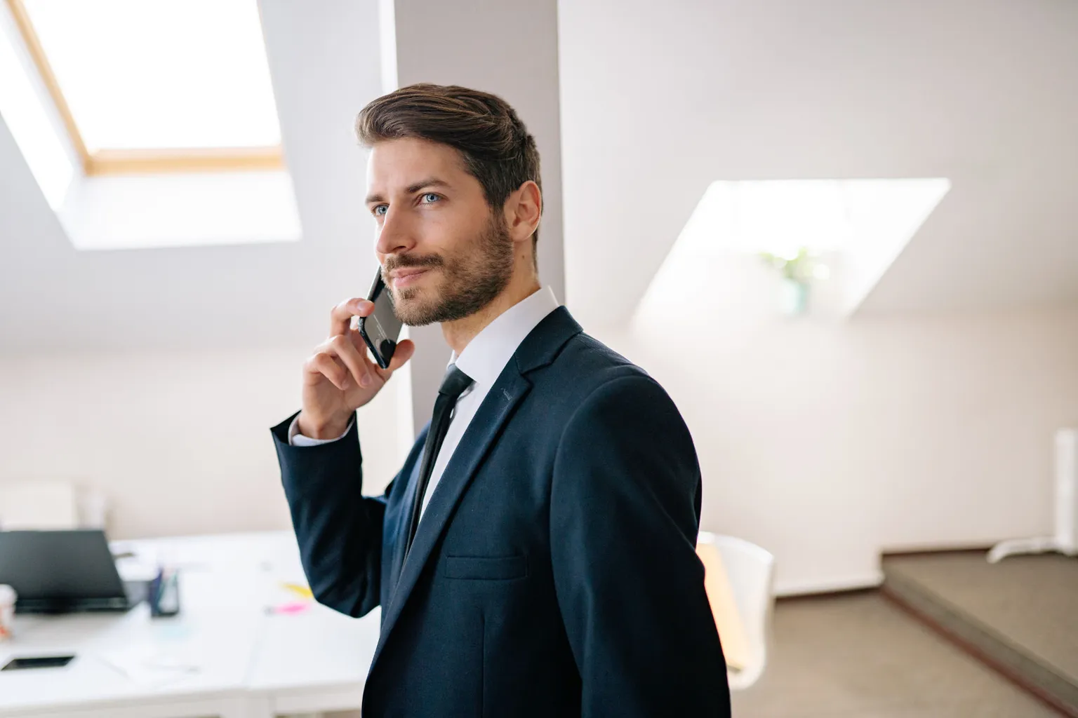 Sales leader in a dark suit taking a call in a bright modern office