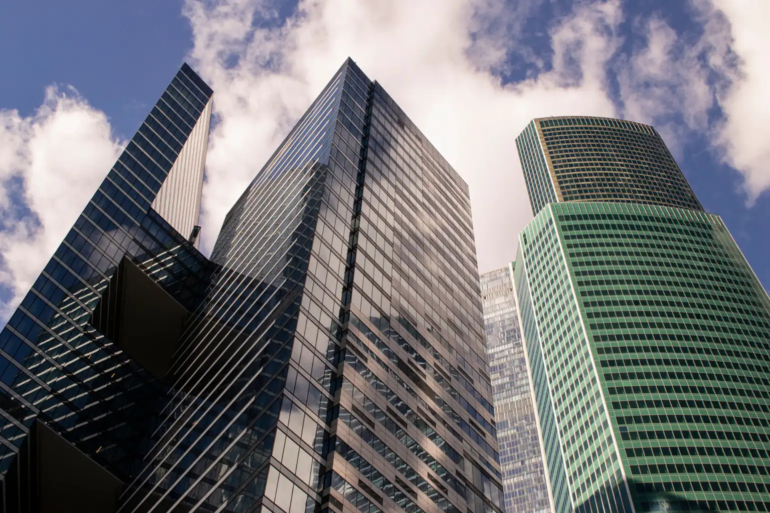 Glass office towers rising against a blue sky with scattered clouds