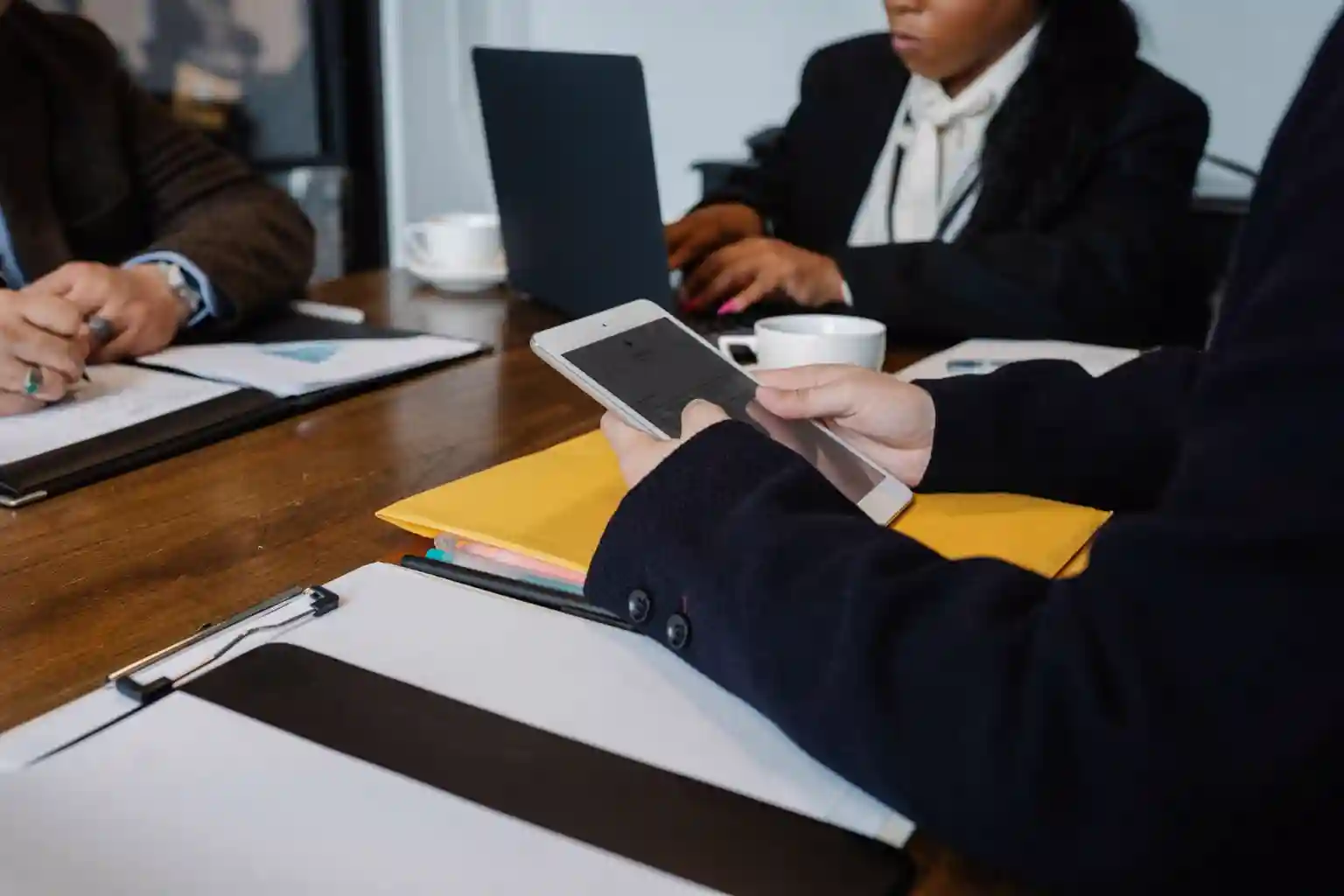 Consultants in a meeting reviewing a tablet and paperwork over a wooden table